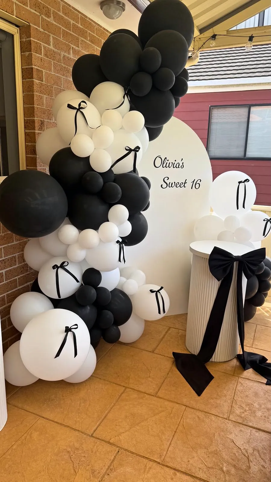 Sweet 16 backdrop with black and white balloons, bows and a custom sign