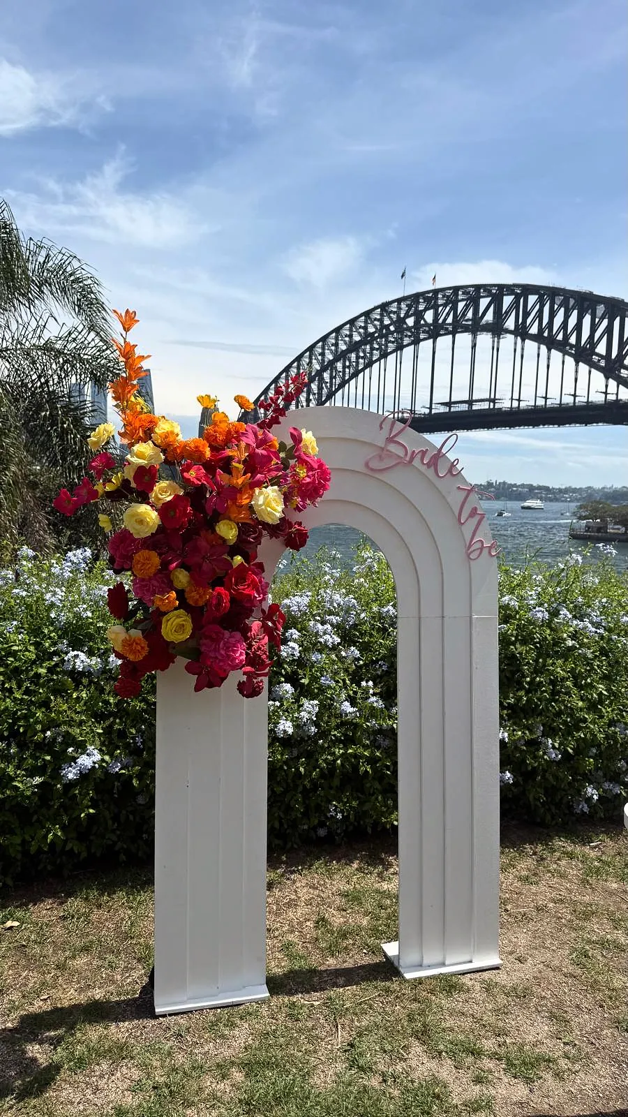 White arch with red, orange and yellow florals, with Sydney Harbour Bridge behind