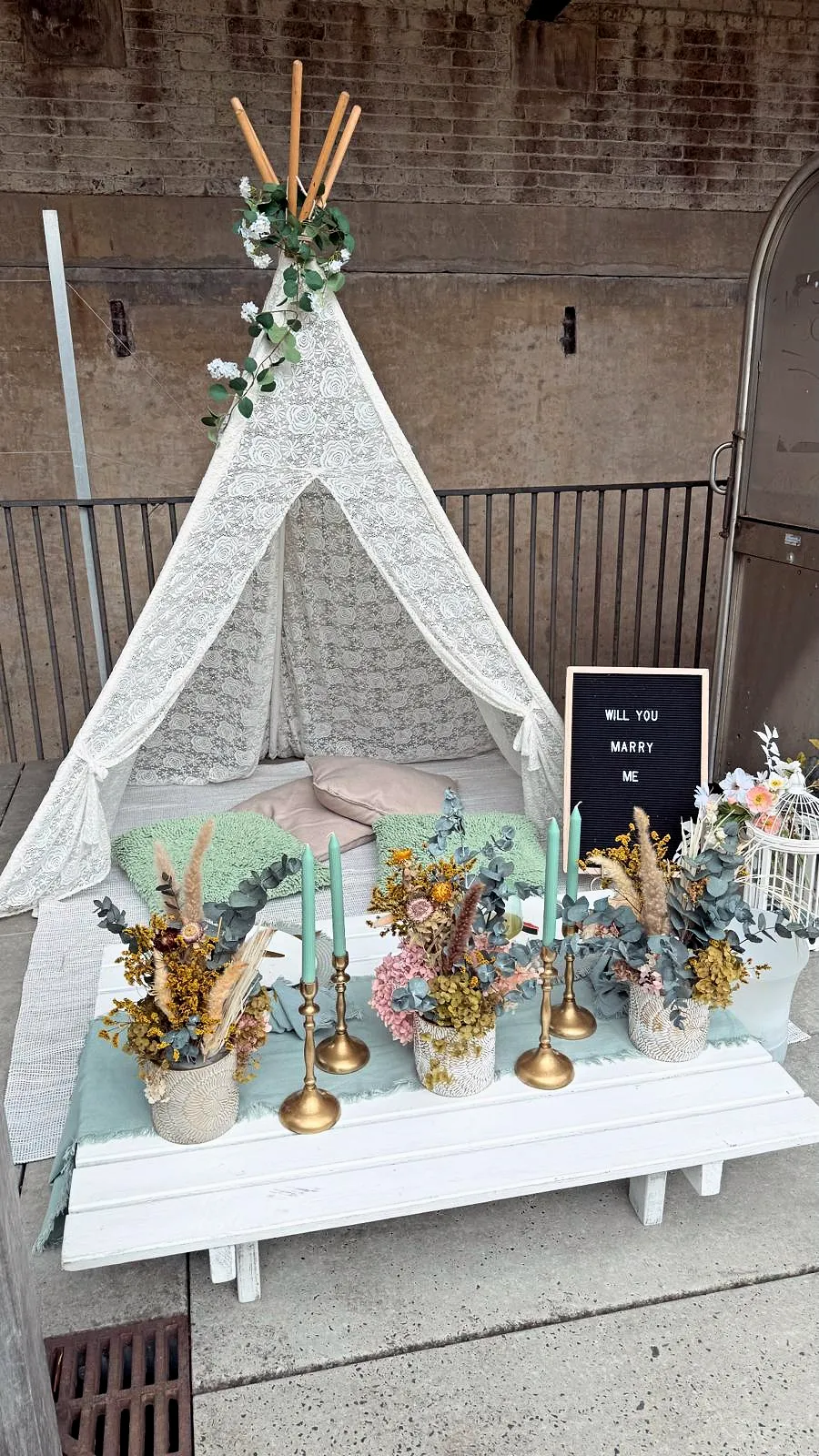 Proposal setup with a lace teepee, sage tablescape and a “Will you marry me” letterboard