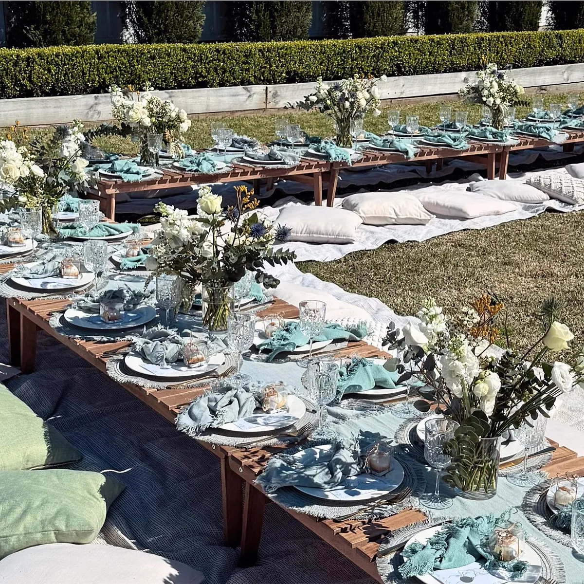 Sage and white picnic tables with white cushions and glassware on a sunny lawn