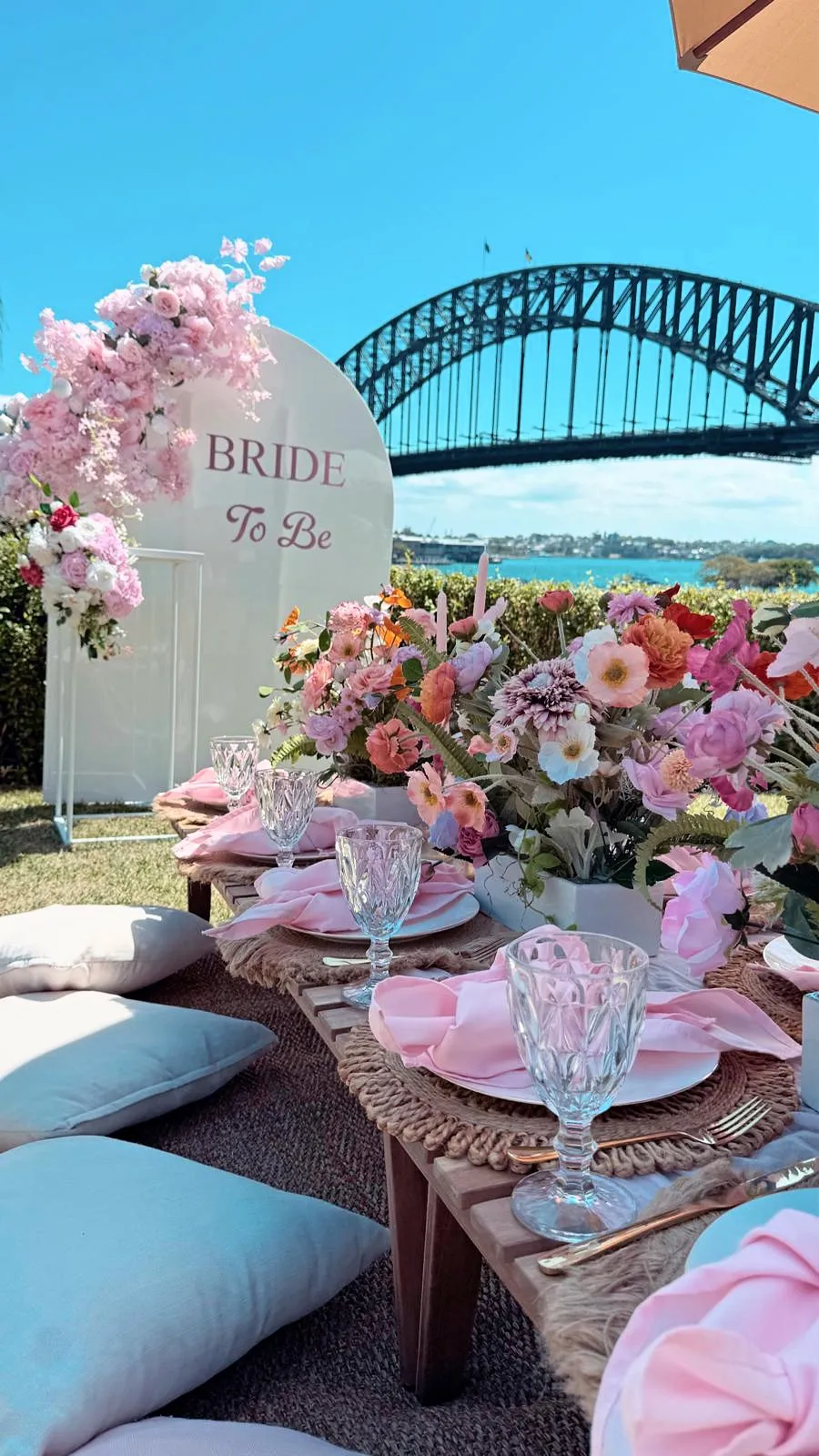 Bride-to-be picnic with a pink floral arch and colourful tablescape, with Sydney Harbour Bridge behind