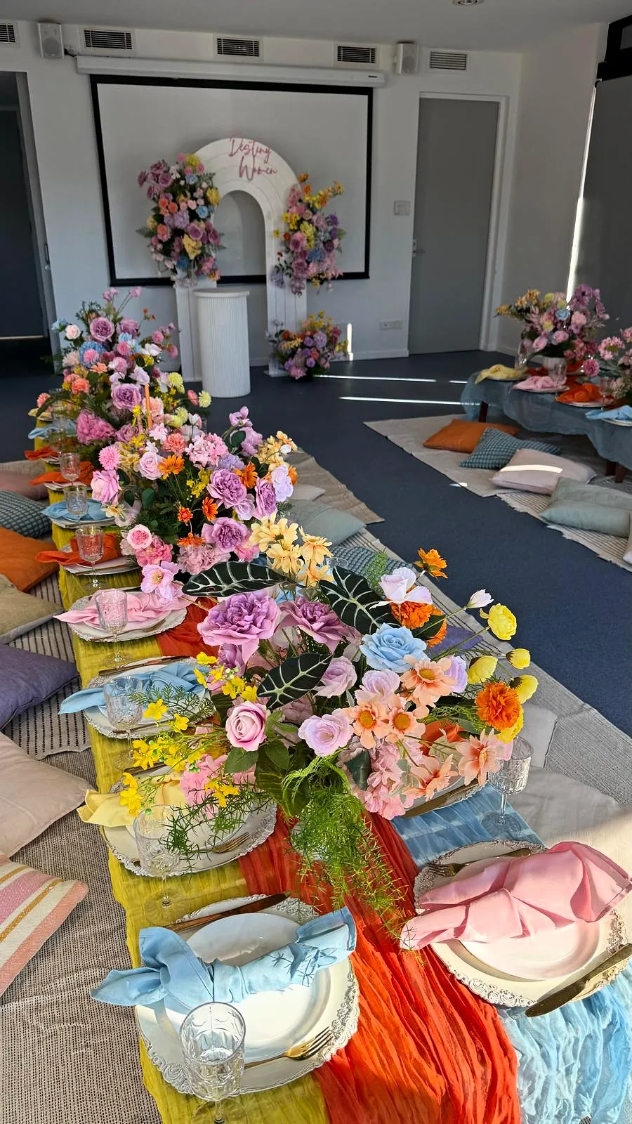 Colourful indoor picnic with bright flowers, orange and blue runners and a floral backdrop