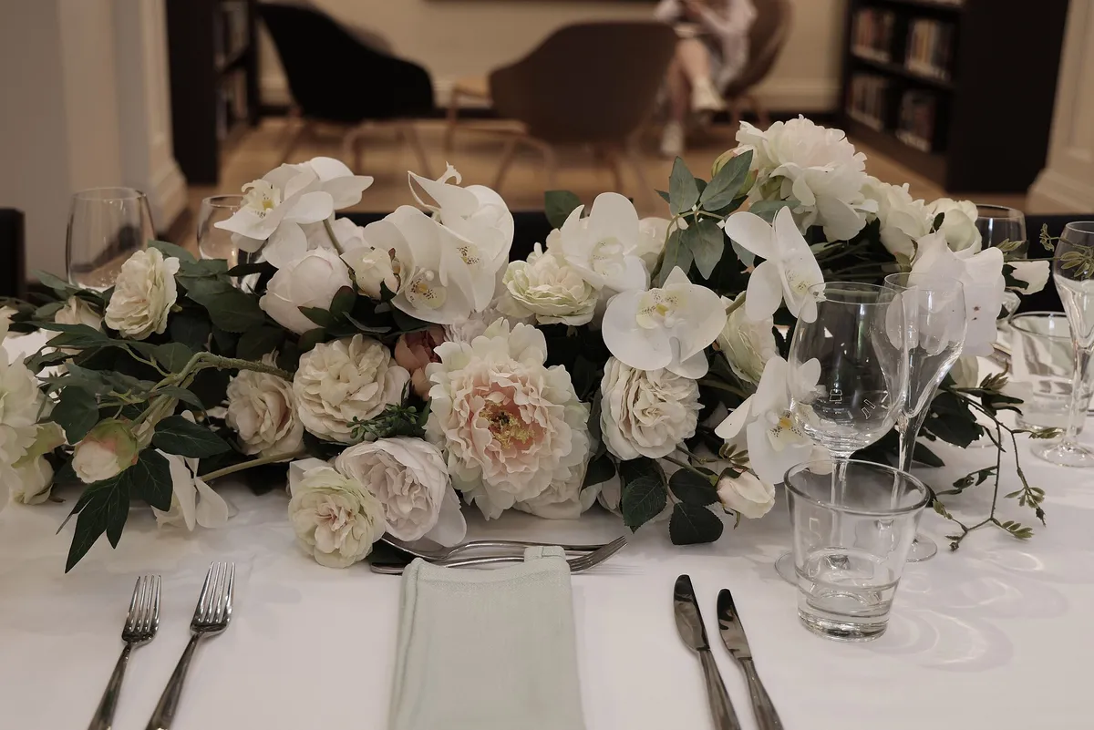 Illustrative wedding table with a long centrepiece of white orchids, peonies and roses