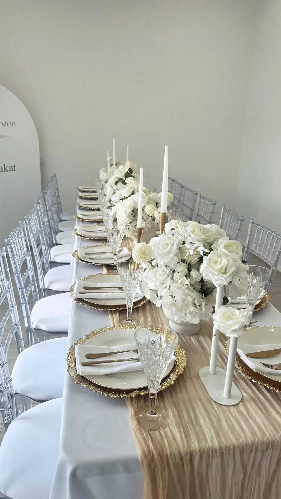 Long white wedding table with white roses, taper candles and a champagne runner