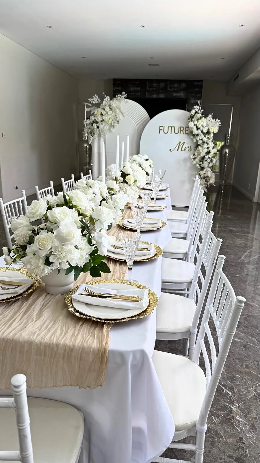 White chairs and a long table with white florals in front of a “Future Mrs” arch