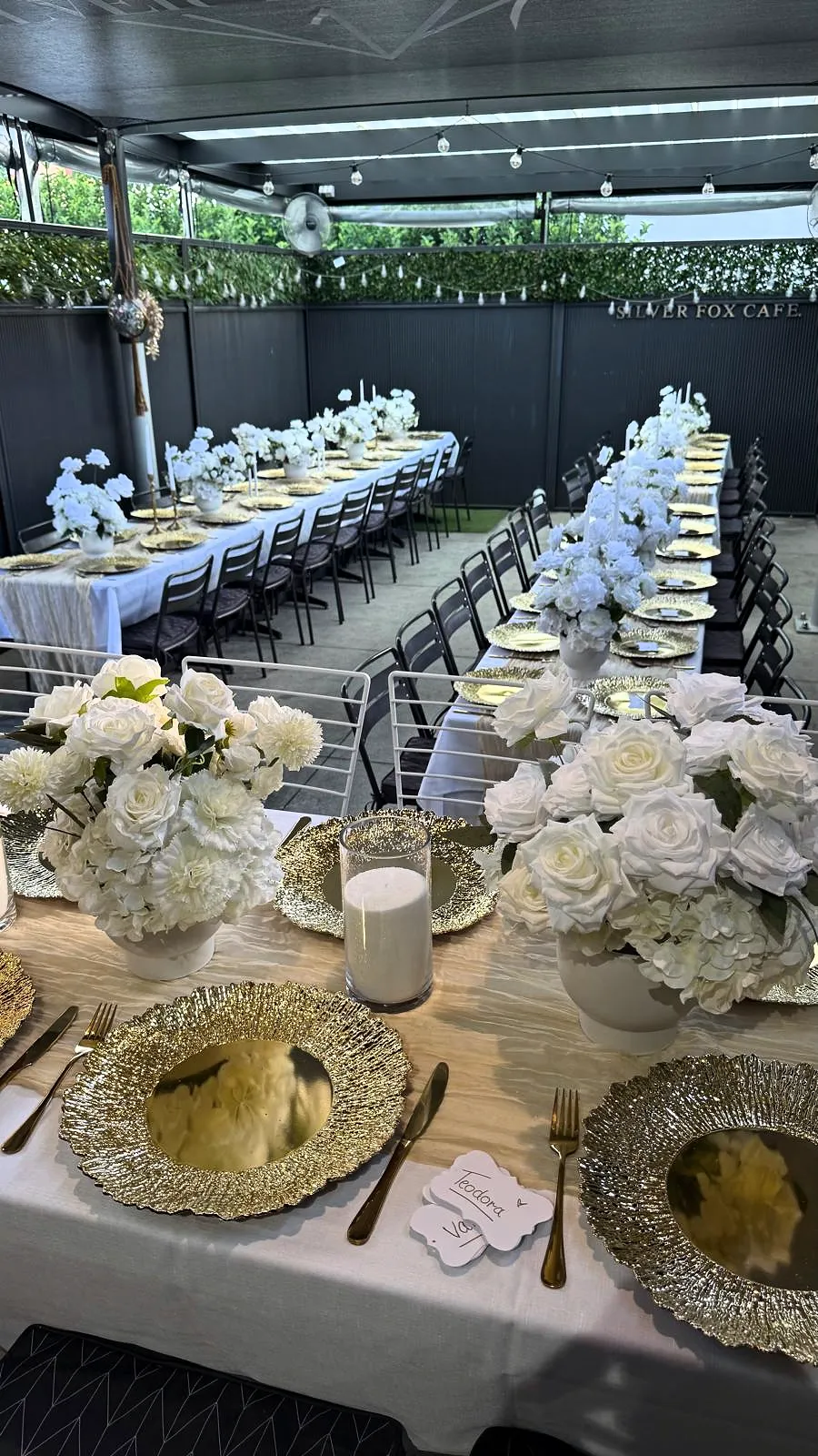 White roses and candlelight on gold charger plates along a long table